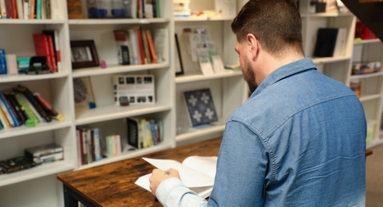 A man is seated at a table, reading a book about supporting family members with addiction.
