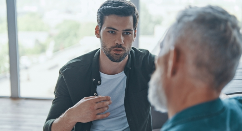 Two men converse in an office, sharing insights on how to assist an alcoholic father effectively.