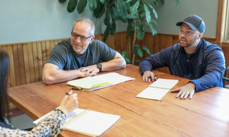 A group of three at a table with notebooks and papers, actively discussing intensive outpatient therapy for addiction.