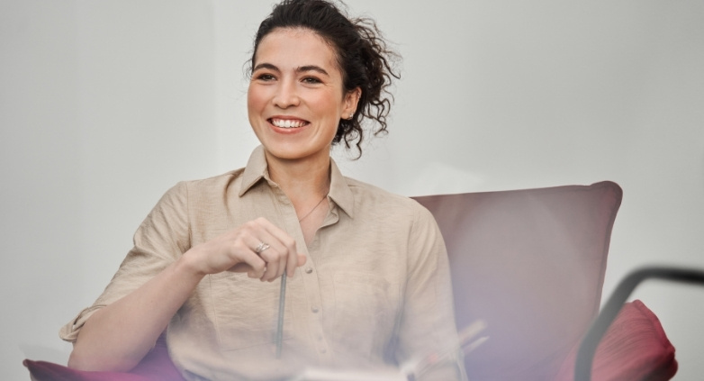 A woman in a chair, smiling warmly, symbolizing hope and encouragement in addiction recovery efforts.