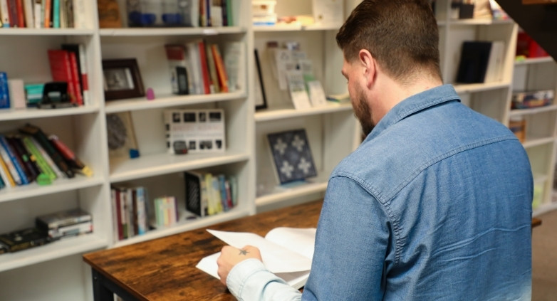 A man at a table focuses on a book discussing self-preservation strategies for helping those with addiction.