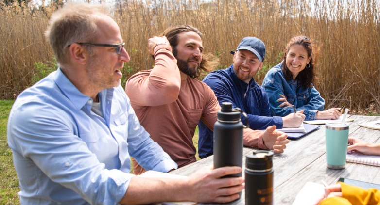 A group of people gathered at a picnic table, discussing support for families of addicts in a therapy setting.