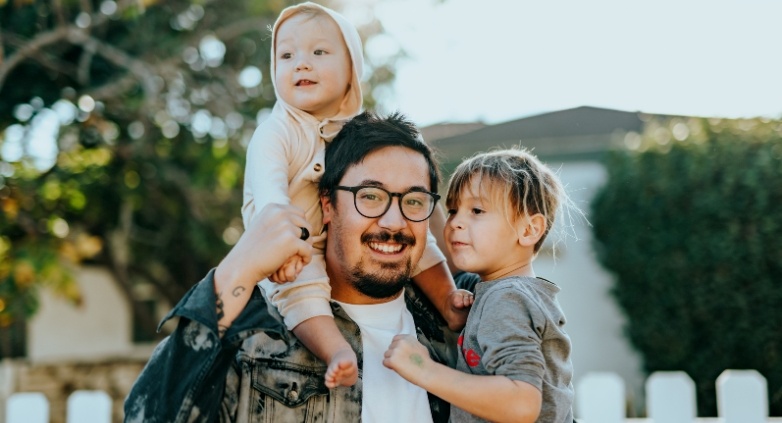 A man with glasses carries a child on his shoulders, symbolizing support and connection in the context of addiction prevention.
