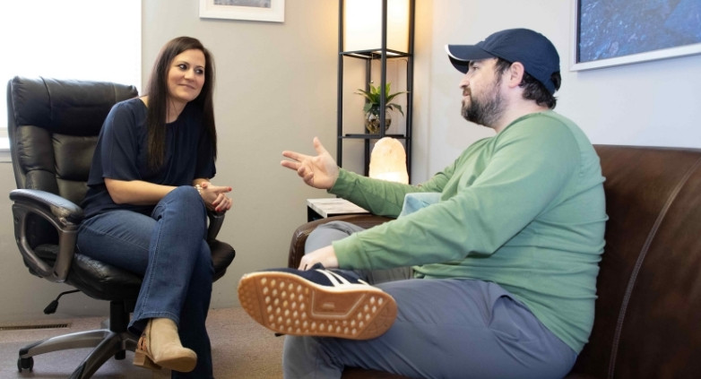 A man and woman sit on a couch, engaged in a conversation about coping strategies for addiction recovery.