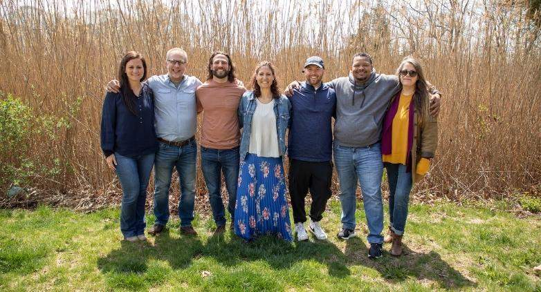 A group of people stands together in front of tall grass, symbolizing support in addiction recovery for families.