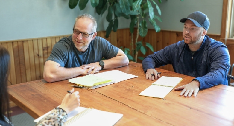 Three individuals, two men and a woman, gather at a table with papers focused on healthy coping strategies for addiction recovery.