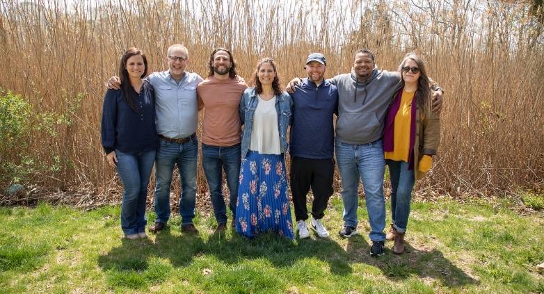 A diverse group of people stands in front of tall grass, focused on strategies to assist an alcoholic family member.