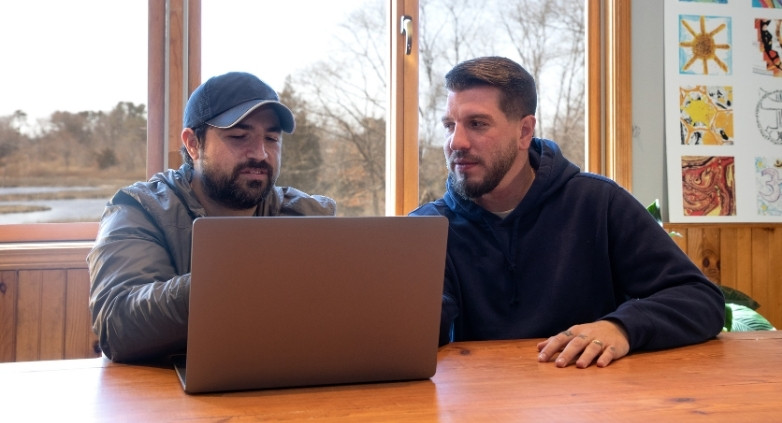 Two men at a table with a laptop, collaborating on ways to assist a family member struggling with alcoholism.