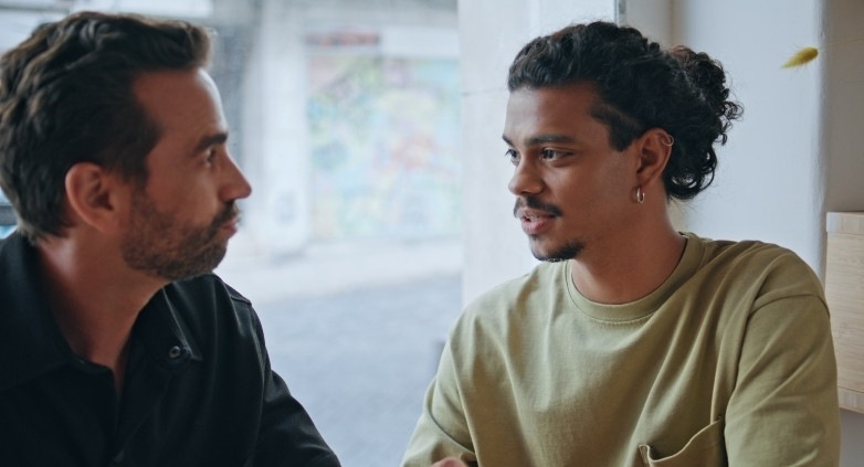 Two men conversing at a table, addressing the topic of helping a son with his drinking issues.