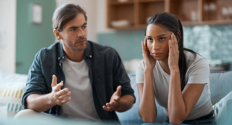 A man and woman sit on a couch, engaged in a conversation about the emotional effects of having an alcoholic parent.