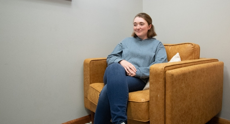 A woman seated in a chair, contemplating self-forgiveness within a room dedicated to addiction recovery.