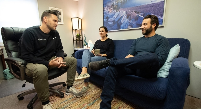 A living room scene with three people on a couch, engaging in a conversation about forgiveness in addiction recovery.