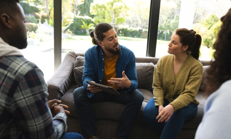 A group of individuals seated on a couch, engaged in conversation during a group therapy session for alcohol abuse recovery.