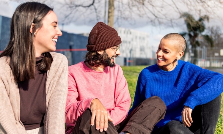 Three young adults are seated on the grass, discussing their experiences in an in-person group therapy for alcohol abuse.