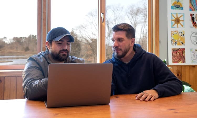 Two men at table with laptop, discussing intensive outpatient therapy for addiction.