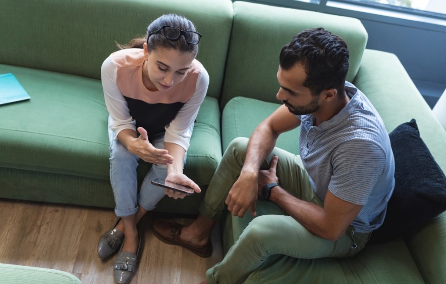 A man and woman sit on a couch, focused on a smartphone, engaging in virtual treatment for addiction.