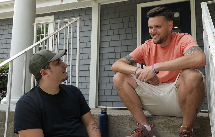 Two men talk on steps, discussing substance use and mental health support.